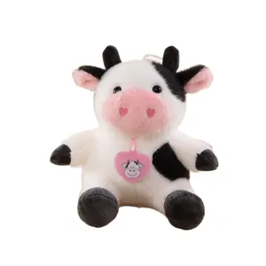 Cute sitting cow plush toy in black and white with pink heart tag and nose details.