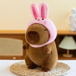 Cute brown Capybara plush toy wearing a pink rabbit hood sitting on a straw mat