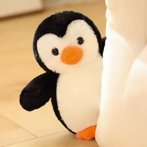 Primer plano de un suave pingüino de peluche asomándose alegremente tras un cojín blanco
