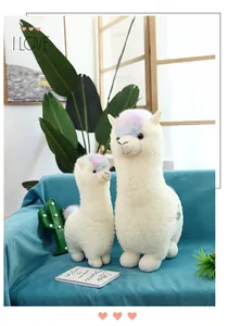 Close-up of adorable white alpaca plush dolls featuring rainbow hair on a teal sofa
