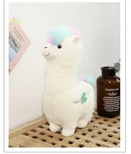 Close-up of cute white alpaca plush toy with rainbow fur and clover detail