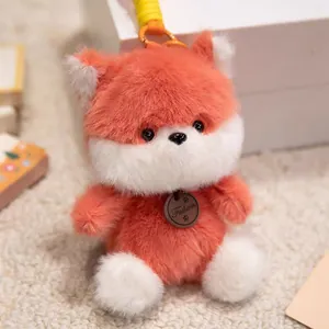 Close-up of a cute orange and white plush fox keychain with soft fur texture and metal tag.