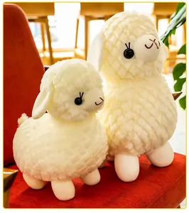 Primo piano di due teneri peluche di alpaca bianchi seduti su una sedia rossa morbida.