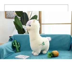 Soft white alpaca plush toy with colorful rainbow mane on blue sofa lifestyle detail