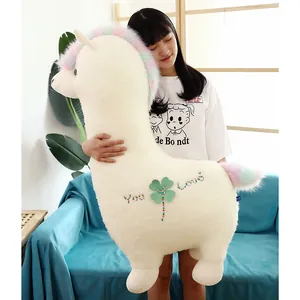 Large white alpaca plush toy with rainbow mane and four-leaf clover held by a girl