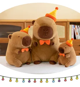 Three sizes of capybara plush toys wearing birthday hats in a cozy home setting.
