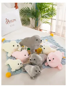 Group of soft plush seal toys in gray, white, and pink on a cozy bed setting.