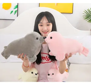 Young woman holding gray and pink simulation plush seal toys in a cozy bedroom setting