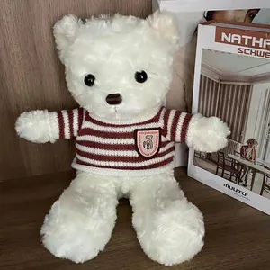 Detailed view of a cute white plush teddy bear wearing a striped maroon knit sweater
