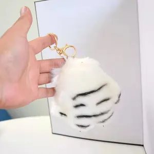 Detail showing a white plush tiger paw keychain with gold-plated metal lobster clasp