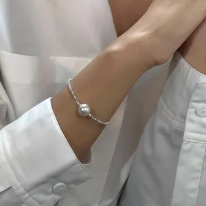 Dettaglio di un gioiello in perline d'argento con una perla lucente su sfondo di camicia bianca