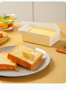 Recipiente blanco para mantequilla con cortador en escena de desayuno con pan tostado
