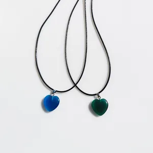 Dettaglio dei ciondoli a forma di cuore blu e verdi su cordoncini neri in stile minimalista