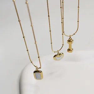 Nahaufnahme goldener Edelstahloberflächen mit Rechteck-, Herz- und Hantelanhängern.