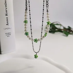 Detail van een dubbellaagse ketting met groene madeliefjeskralen en witte parels.