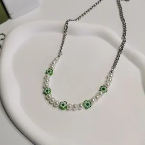 Close-up van groene madeliefjesketting met witte parels en zilveren kettingdetail.