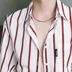 Detailed view of a silver titanium steel necklace on a model wearing a striped shirt