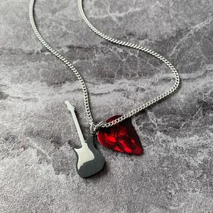 Dettaglio dei ciondoli a forma di chitarra e plettro rosso marmorizzato su catena argento