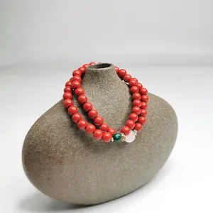 Detailansicht eines zweireihigen zinnoberroten Perlenarmbands auf einer Zen-Keramikvase