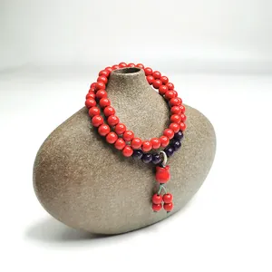Detailansicht eines roten Zinnober-Doppelarmbands mit Anhänger auf einer Vase