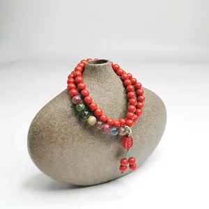 Detail eines Armbands aus rotem Zinnober mit bunten Perlen und einem Glücksanhänger