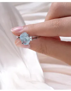 Detailaufnahme eines Roh-Aquamarin-Rings mit S925-Silberband, von Fingern gehalten.