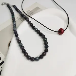 Vue détaillée du collier en perles de pierre naturelle et du collier noir avec perle rouge.