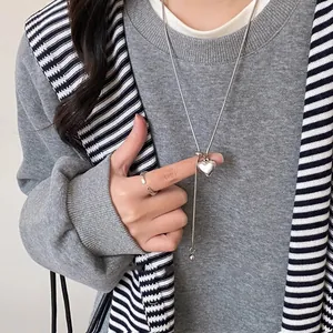 Nahaufnahme einer minimalistischen silbernen Herz-Halskette auf grauem Strickpullover