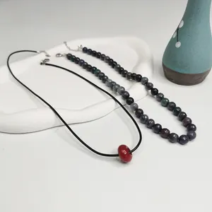 Détail de colliers de style chinois moderne avec perles en pierre naturelle et perle rouge.