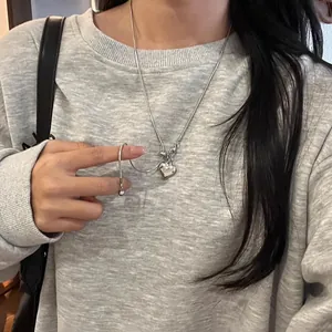 Nahaufnahme einer silbernen Herz-Halskette mit verstellbarem Schiebeverschluss auf grauem Pulli.