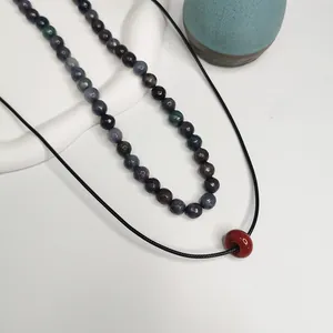 Gros plan de perles en pierre naturelle facettée et pendentif rouge sur collier.