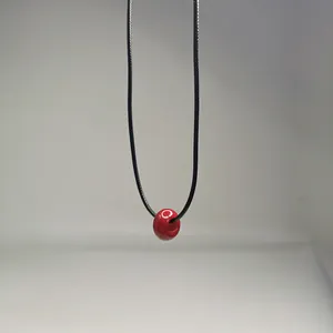 Gros plan d'une perle en pierre naturelle rouge sur un collier en cordon noir simple