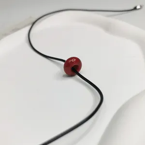 Gros plan d'un collier minimaliste avec une perle en pierre rouge sur un cordon noir.