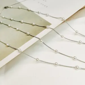 Detailed macro view of a silver-colored chain necklace featuring spaced white pearls