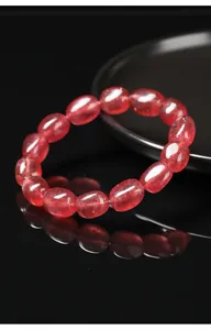Primer plano de una pulsera de cuarzo fresa natural con cuentas ovales sobre fondo negro espejo