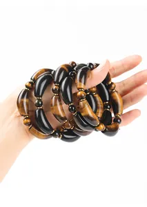 Macro detail of natural yellow tiger eye and obsidian curved tube bead bracelet on hand.