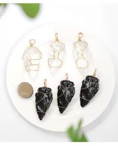 Detail of handmade wire-wrapped clear and black raw crystal arrowhead pendants on white plate