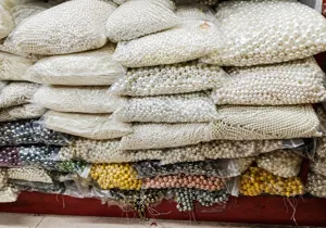 Bulk assorted white and colored shell pearls in transparent bags for DIY jewelry.