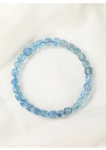 Detailopname van een ijsblauwe aquamarijn armband op een witte getextureerde stoffen achtergrond