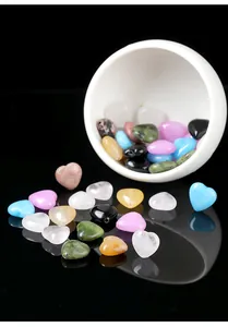 Close-up detail of heart-shaped natural stone beads falling from a white ceramic bowl.