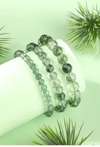 Gros plan de bracelets en perles de quartz fantôme vert sur un support cylindrique blanc