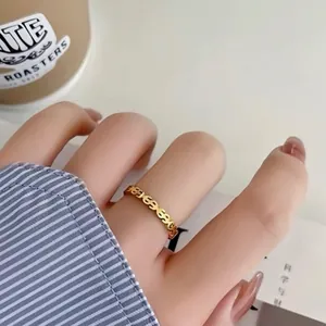 Detail view of a golden stainless steel ring featuring an open dollar sign pattern.
