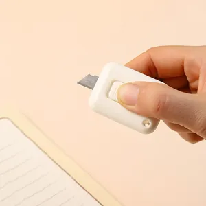 Primer plano detallado de un mini cúter blanco portátil sostenido por una mano sobre un cuaderno