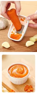Manual ginger and garlic grater creating smooth carrot puree on a wooden cutting board