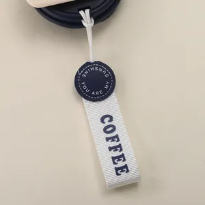 Detailaufnahme der weißen Handschlaufe mit COFFEE-Schriftzug und blauem Anhänger