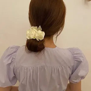Close-up view of elegant cream white silk rose hair scrunchie for retro bun styling