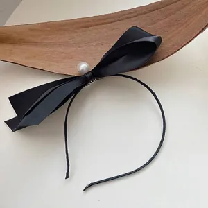 Close-up detail of a chic black ribbon bow headband with a white pearl accent