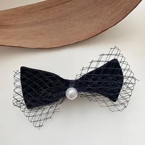 Close-up of elegant black velvet bow hair clip with mesh wings and pearl center.