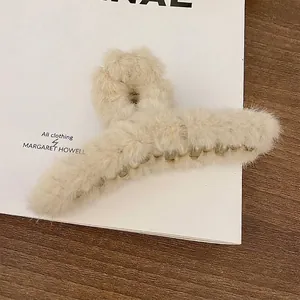Detailed close-up of a soft beige fuzzy lambswool hair claw clip on paper background