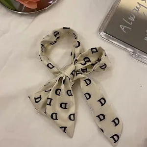 Gros plan d'un ruban à cheveux en soie crème avec imprimé monogramme lettre D noir